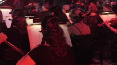 Müzisyenler Çello ve Keman Müzik Kitapları Standları İnsanlar Backs Kırmızı ve Mavi Aydınlatma Dark Hall Rock Senfoni Konser Ukrayna Tur Kiev oynuyor