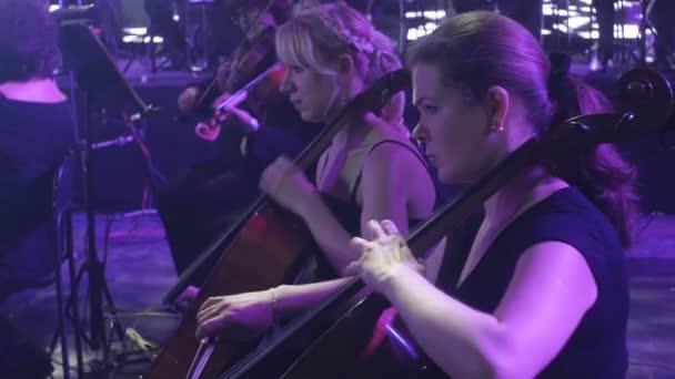 Rock Symphony Concert gira ucraniana Kiev director Nikolai Lysenko violonchelistas femeninas en primer plano músicos están tocando libros de música en soportes luces — Vídeos de Stock