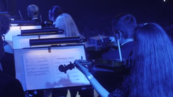 Musiker spielen Geigen mit einem Bogen Menschen Rücken Notenbücher auf Ständen Beleuchtung Dark Hall Rock Symphonie Konzert ukrainische Tour — Stockvideo