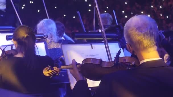 Rock symfoni konsert Kiev ledare av bandet långhåriga mannen musiker spelar violiner män och kvinnor med en bågar tittar på musik böcker kameraman — Stockvideo
