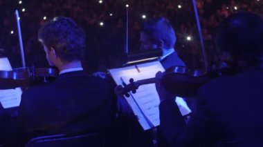 Müzisyenler kemancı Mavi ışıklar müzik kitap standları aydınlatma, karanlık Hall görüntüleyicilerde onların koltuk Rock Senfoni üzerinde oturan bir yay ile oynuyorlar