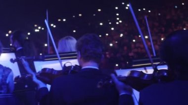 Müzisyenler kemancı Mavi ışıklar müzik kitap standları aydınlatma, karanlık Hall görüntüleyicilerde onların koltuk Rock Senfoni üzerinde oturan bir yay ile oynuyorlar