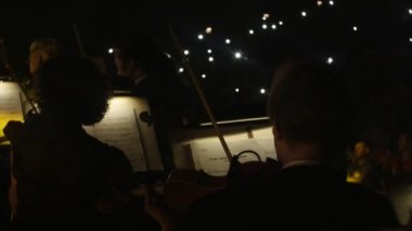 Müzisyenler erkekler karanlık Hall ışıklar müzik kitap standları Are içinde Keman çalmaya ışıklı Rock Senfoni konser Ukrayna izleyiciler bir koltuğa oturan