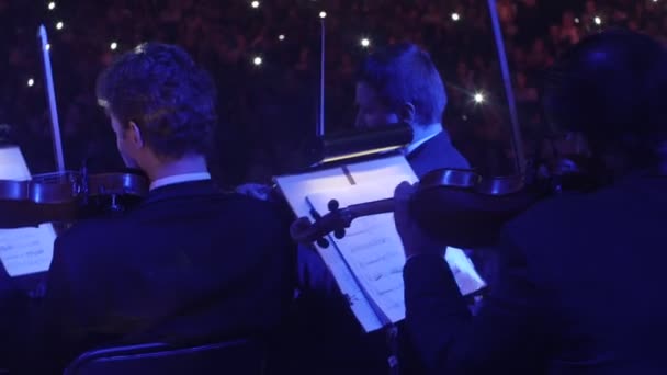 Musikerna violinister spelar med en bågar blåljus musikböcker på står belysningen i mörk Hall tittarna sitter på sina platser Rock Symphony — Stockvideo