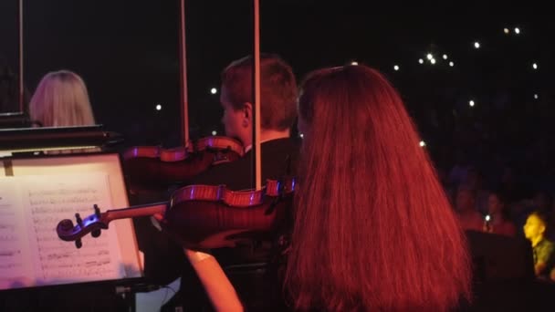 Müzisyenler kemancılar uzun saçlı erkek izleyiciler kendi koltuk müzik kitap standları aydınlatma karanlık salonda oturan kırmızı ışıklar iletken oynuyorlar — Stok video