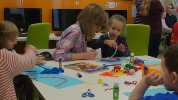 Mujer joven y niño están haciendo un arco iris-apliques en una hoja azul de papel pegando un blanco hilos niños y niñas personas están haciendo un hecho a mano productos — Vídeos de Stock