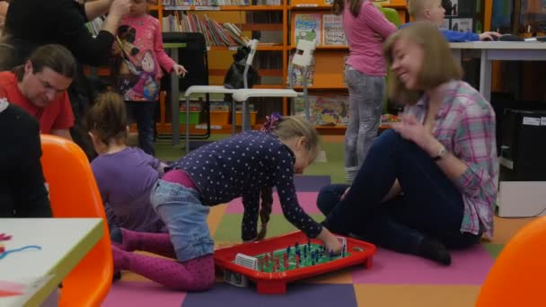 Famiglia Master Class in Opole Biblioteca Bambino Bambina Stood up Giocando a hockey da tavolo con insegnante seduto su un pavimento Giovane donna sorride bambini sono intorno — Video Stock