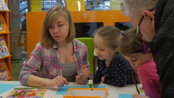 Familie Meisterkurs Opole Bibliothek junge Frau nimmt einen Stift und Zeichnung auf einem blauen Papier Kinder suchen grauhaarige Mann kommt Menschen machen ein Geschenk — Stockvideo