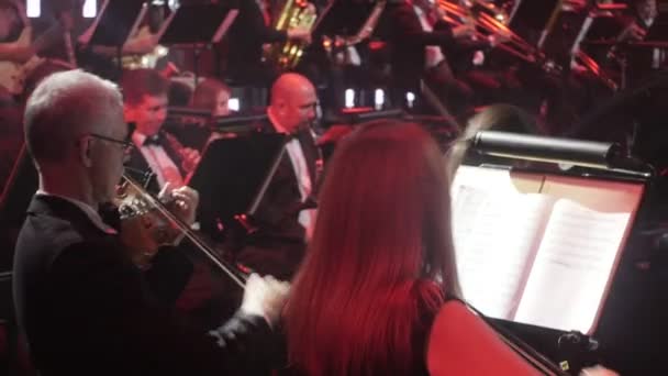Symfonický koncert ukrajinském turné Kyjev dirigent Nikolai Lysenko hudebníky hrají housle a větry hudbu knihy na stojany osvětlení tmavé Hall — Stock video
