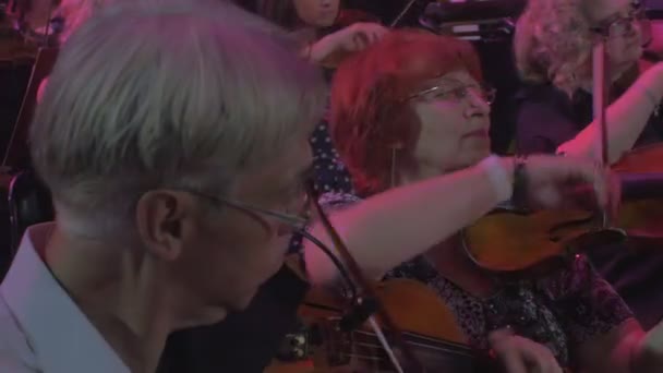 Concierto Sinfónico de Rock Kiev Grupo de Violinistas Senior Aged Woman toca y sonríe a jóvenes músicos Libros de música en stands Iluminación Dark Hall — Vídeo de stock