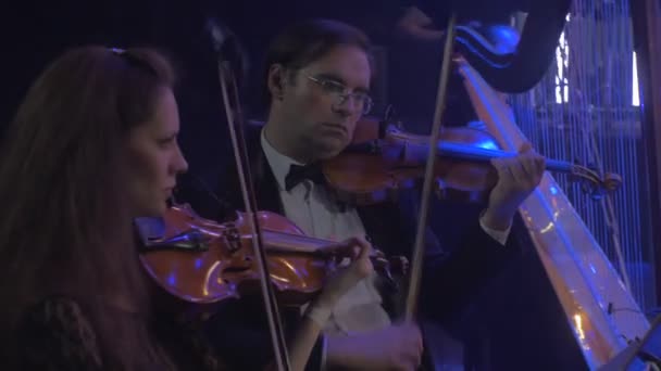 Concert symphonique rock Kiev Groupe de musiciens jouant du violon Harpiste Livres de musique sur les supports Lampes bleues Illumination Violoniste masculin joue sérieusement — Video