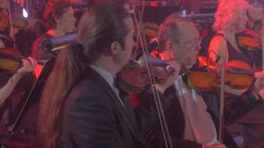Rock Senfoni konser Kiev kemancılar siyah önlük iyi-Dressesd erkek ve kadınlarda bir satır kırmızı ışıklar aydınlatma karanlık salonda oturmuş keman oynuyorlar