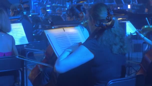 摇滚交响音乐会基辅大提琴手在看台蓝灯照明上扮演他们一部分妇女在晚礼服全景乐团音乐书籍 — 图库视频影像