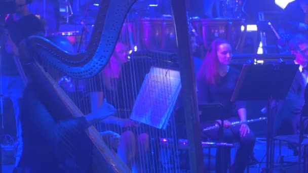 Rock symfoni konsert Kiev Harpist är spela plockning strängar kvinnliga flöjtisten väntar för hennes parti grupp av musiker spelar musikböcker på stativ — Stockvideo