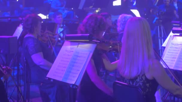 Rock Symphony Concert Kiev Cameraman está filmando violinistas Grupo de músicos Homens e mulheres estão tocando livros de música em suportes Lâmpadas azuis Iluminação — Vídeo de Stock