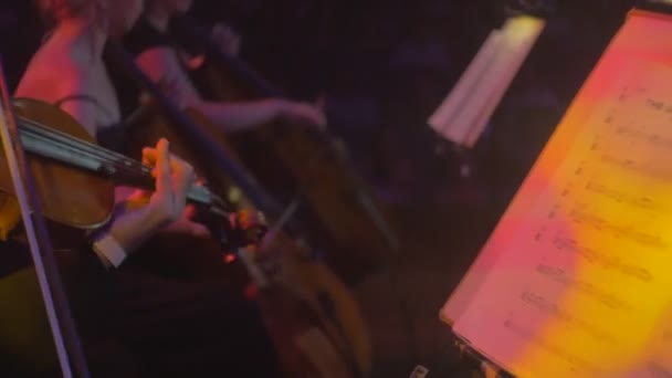 Ροκ συμφωνική συναυλία Κίεβο βιολιστής τσελίστες βιβλίο μουσικής στο ζωηρόχρωμο κόκκινο και κίτρινο φως μουσικοί παίζουν σκοτεινή αίθουσα Συμφωνική Ορχήστρα επιδόσεις — Αρχείο Βίντεο