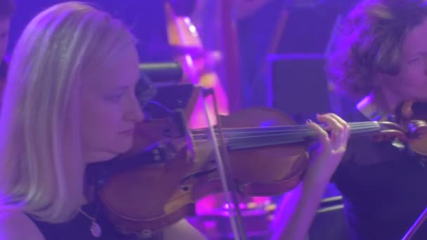 Rock Senfoni konser Kiev kemancılar sarışın kadın uzun saçlı adam iyi giyimli müzisyenler müzik kitap standları aydınlatma karanlık Hall üzerinde oynuyorlar — Stok video