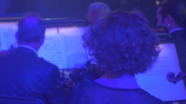 Müzisyenler keman uzun saçlı adam mavi ışık müzik kitap standları kemancılar, karanlık Hall görüntüleyicilerde Rock Senfoni konseri, gerçekleştirdiğiniz oynuyorlar