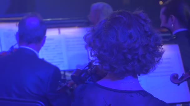 Muzikanten zijn langharige Man violen blauwe lichte muziekboeken over Stands violisten in Dark Hall kijkers bij Symphony rockconcert uitvoert — Stockvideo