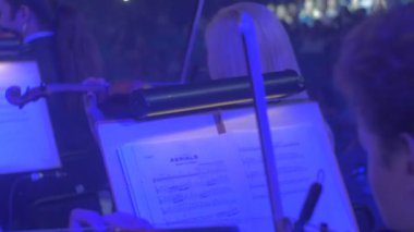 Erkek ve dişi kemancılar iyi giyimli müzisyenler keman mavi ışık notlar Are içinde Rock Senfoni konser Kiev, standları karanlık Hall izleyiciler üzerinde oynuyorlar