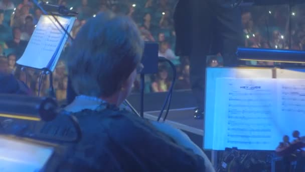 摇滚交响音乐会基辅精心打扮的音乐家正在演奏弓形乐器指挥在Tuxedo音乐书籍在看台上的观众人群照明 — 图库视频影像