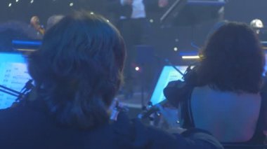 Orkestra şefi ve kemancı izleyiciler dalga çakmak iyi giyimli müzisyenler yavaş melodi ile keman müzik kitap standları aydınlatma karanlık Hall üzerinde oynuyorlar