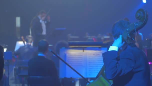 Rock Symphony koncert Kiev hosszú hajú férfi vezeti a csellisták jól öltözött zenészek játszanak meghajolt Instruments megjegyzések standok Lights Dark Hall — Stock videók