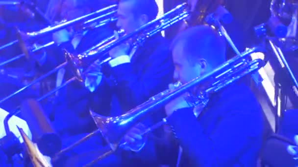 Concierto Sinfónico de Rock Kiev Hombres tocando trompetas con luz roja Jóvenes músicos bien vestidos están tocando libros de música en soportes Iluminación en pantallas — Vídeos de Stock