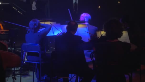 Muzikanten Silhouettes dirigent leidt de violisten mensen spelen muziekboeken worden belicht op Stands verlichting Dark Hall Symphony Orchestra — Stockvideo