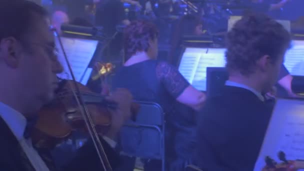 Музыкальный оркестр скрипачей Киевского симфонического концерта "Рок-симфония" играет ноты к музыкальным инструментам на подсвечниках на экранах Темного зала — стоковое видео