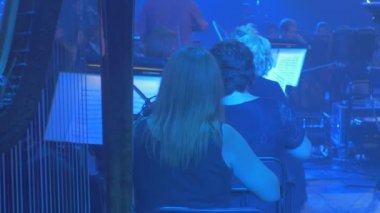Müzisyenler keman Arpçı Bun Panorama orkestra dizeleri aletleri mavi lambalar karanlık salon kitap ile standları müzisyen arka Rock Senfoni üzerinde oynamak.
