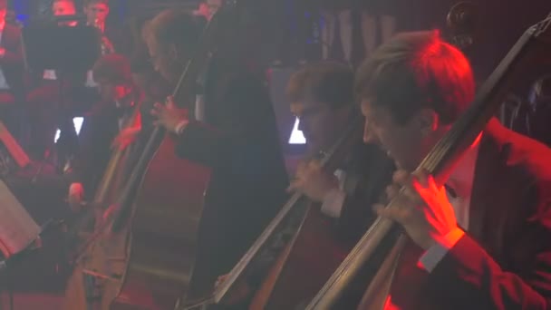 Concerto sinfonico rock I violoncellisti concludono la parte I musicisti suonano archi bassi Strumenti La luce esce Musica ritmica Lampade blu Sala oscura Libri sugli stand — Video Stock