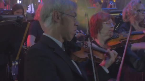 Rock Symphoniekonzert Kiewer Geiger panorama junge und ältere Musiker Männer Frauen spielen Geigen rhythmische Musik Saiteninstrumente blaue Lampen — Stockvideo
