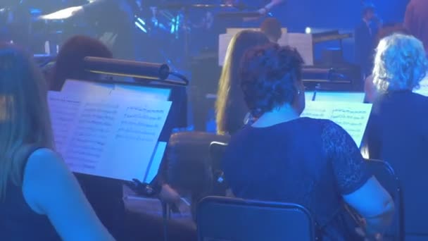 Muzikanten spelen violen panorama van de orkest snaren gebogen instrumenten blauwe lampen donkere Hall boeken op stands muzikant Backside Rock Symphony concert — Stockvideo