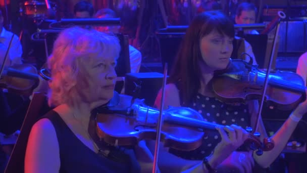 Rock Symphony koncert poważnych skrzypków muzycy Play Violins kobiety w suknie wieczorowe grać smyczki instrumenty niebieskie i czerwone lampy oświetlenie Dark Hall — Wideo stockowe