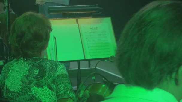 Müzisyenler keman prova iletken müşteri adayları dize aile eğdi aletleri mavi ve yeşil lambaları aydınlatma karanlık Hall kitap standları Rock Senfoni üzerinde oynamak — Stok video