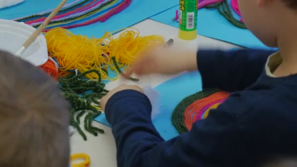 Dziecko jest oddzielenie bawełny kawałki do kleju to niebieski papier chmury niebo dla dzieci ręce robią Rainbow z kolorowe nici siedzi w klasie tabeli — Wideo stockowe