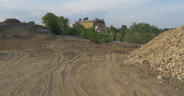 Straße zur Zementfabrik durch Haufen von Granitstaub Betonwerk keine Menschen an langweiliger Industrielandschaft sonniger Abend Bau der Anlage unter grünen Bäumen — Stockvideo