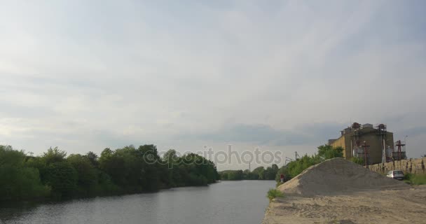 Zementwerk am Ufer der Flusslandschaft Bäume auf der anderen Seite Betonwerk in sonnigen Abend glattes Wasser Gebäude Haufen von Granitstaub bewölkten Himmel — Stockvideo