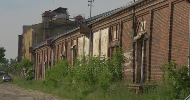 Antiguo muro de ladrillo de fábrica abandonado coche de construcción está estacionado aburrido paisaje industrial soleado noche estructuras de la planta entre árboles verdes cielo nublado — Vídeo de stock