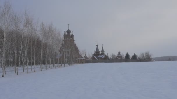 Sviatogorskaya Lavra と雪に覆われた冬の白樺ツリー路地沿いに近づいているすべての聖徒のスキットと呼ばれるキリスト教木製修道院 — ストック動画