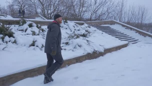 Un homme barbu descendant un escalier d'hiver enneigé, et se déplaçant à l'Artyom Monument de 1927, qui est de vingt mètres de haut dans les crépuscules du soir — Video