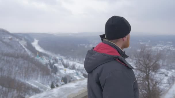 Ein Mann mittleren Alters steht am Artjom-Denkmal (1927) und blickt von seiner Aussichtsplattform auf die Swjatogorskaja lavra in den schneebedeckten Bergen. — Stockvideo