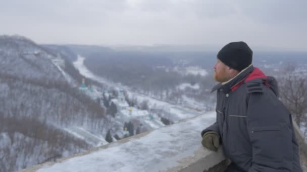 Un hombre barbudo religioso que mira a Sviatogorskaya Lavra, situado en pintorescas montañas, desde la cubierta de observación del monumento de Artyom en invierno — Vídeo de stock