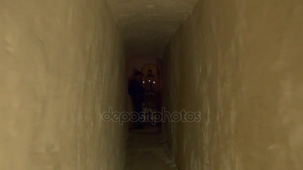 Un couloir étroit dans la grotte orthodoxe de la craie et un homme priant devant sainte Marie icône et trois bougies allumées en Svyatogorskaya Sainte Lavra — Video