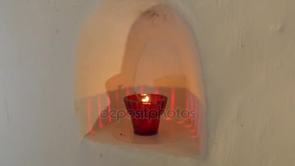 Una vela votiva roja colocada en un arco de tiza blanca, situado en un corredor de tiza Semidark tallados sagrados de Sviatogorskaya Lavra en invierno — Vídeo de stock