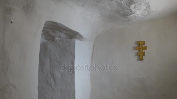 Un couloir étroit blanc austère avec une grande croix et une bougie votive rouge placée dans une arche dans les grottes de craie de la lave orthodoxe de Sviatogorskaya en hiver — Video