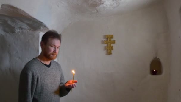 Um homem religioso de meia-idade vai ao longo de um corredor estreito branco para um cameraman com uma vela do lit em sua mão em um temple da caverna do giz no inverno — Vídeo de Stock