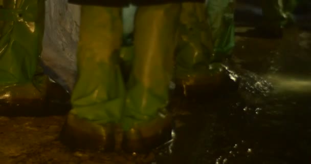Ботинки в химическом костюме на ногах людей с крупным планом, который сделан в глубоком старом тоннеле, пол которого покрыт грязной черной водой — стоковое видео