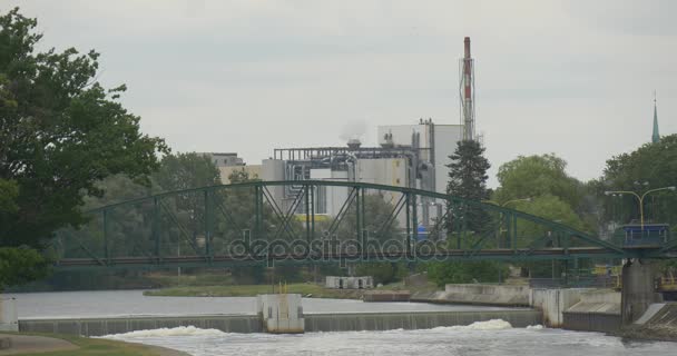 Saai industriële landschap brug Over rivier Man wandeling langs de brug pijpen van een fabriek worden op de achtergrond groene verse bomen in bewolkte dag eenzaamheid — Stockvideo